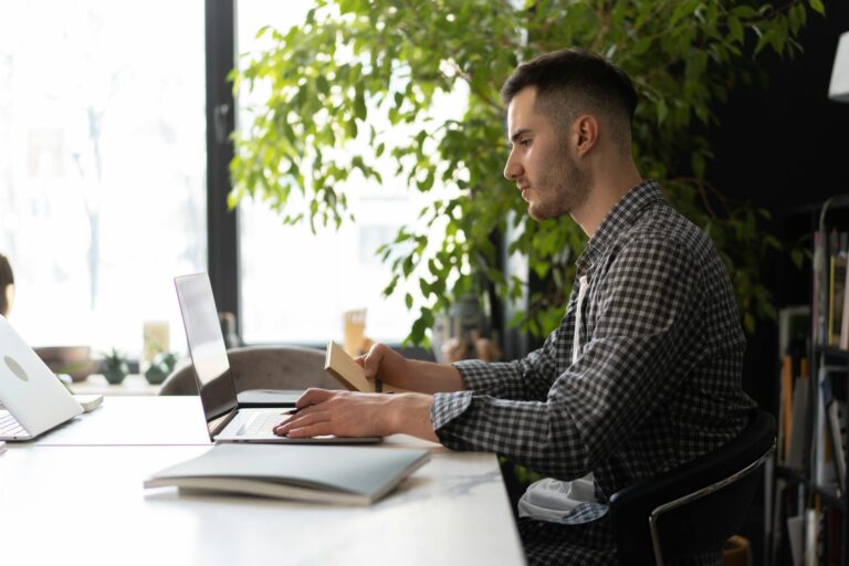 A focused person working at a laptop in a quiet, sunlit workspace