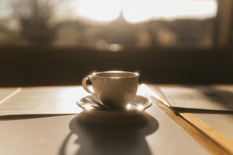 A coffee cup beside a window catching the early morning sun, calm and warm